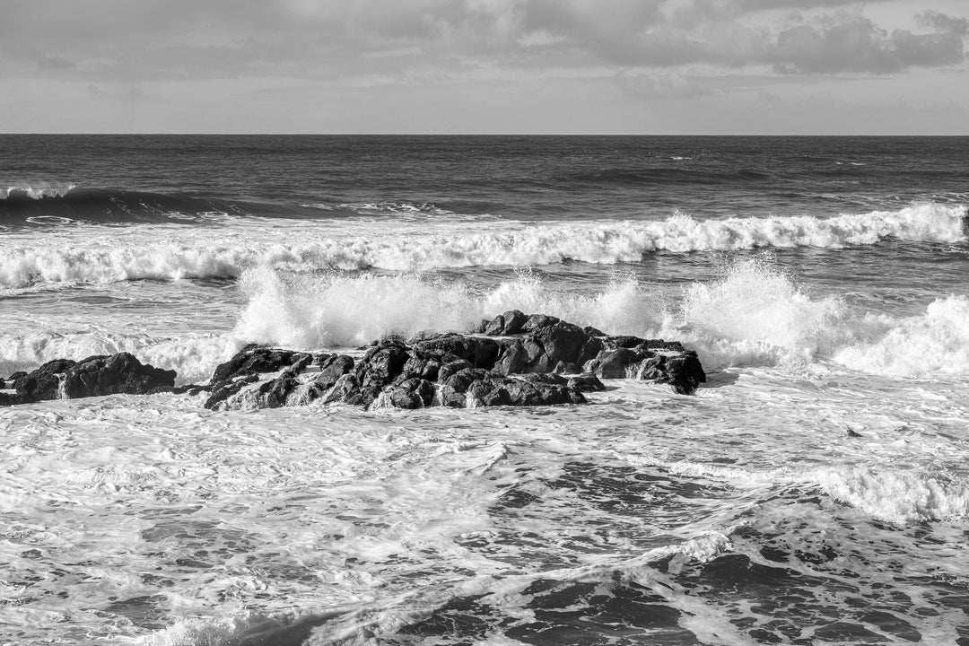 Black and white photo of waves crashing against rocks in the ocean.