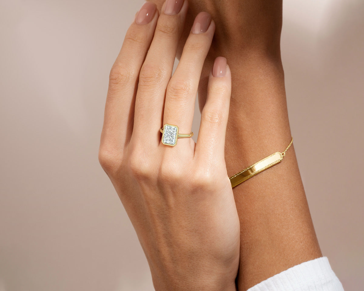 woman's hands with beautiful yellow gold emerald solitaire engagement ring and a gold bracelet