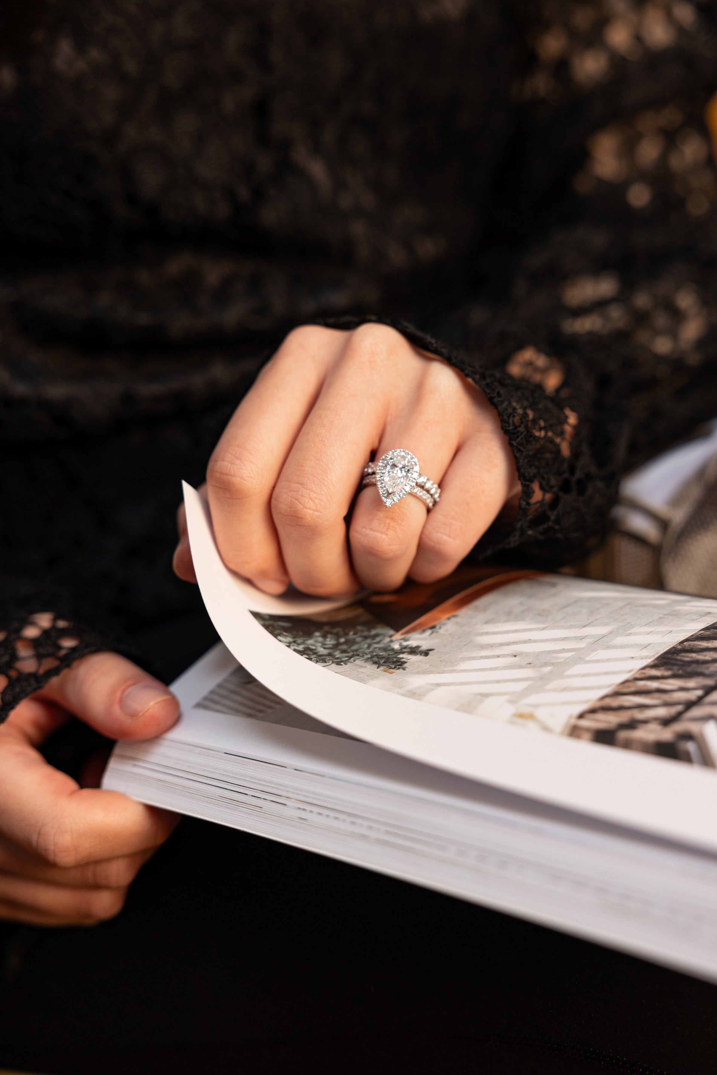 woman browsing a magazine wearing stunning pear shaped engagement ring and diamond pave wedding band