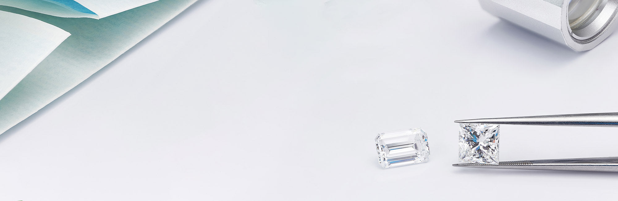emerald and radiant diamonds on a white background held in tweezers