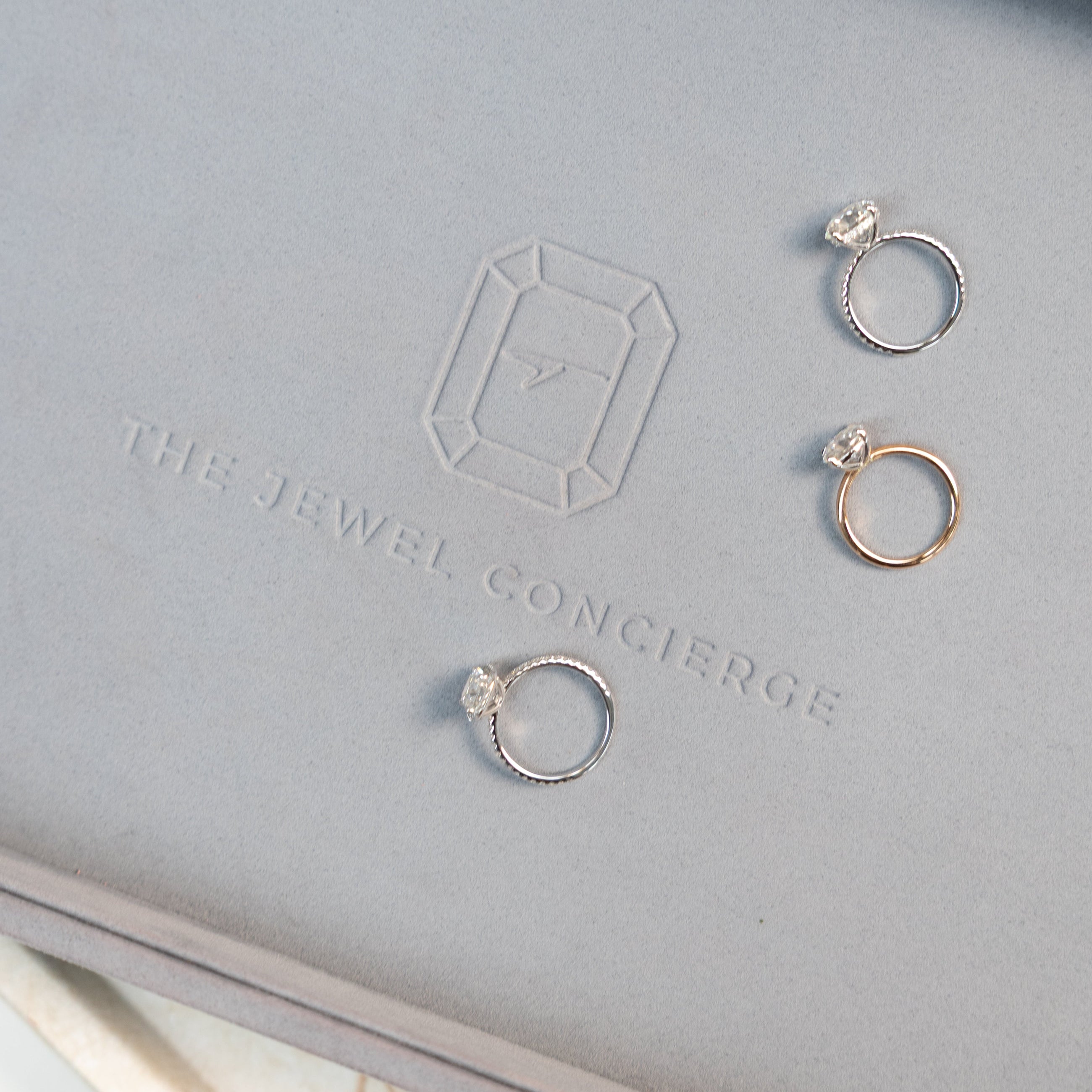 Three diamond rings on a jewellery tray with 'The Jewel Concierge' branding.