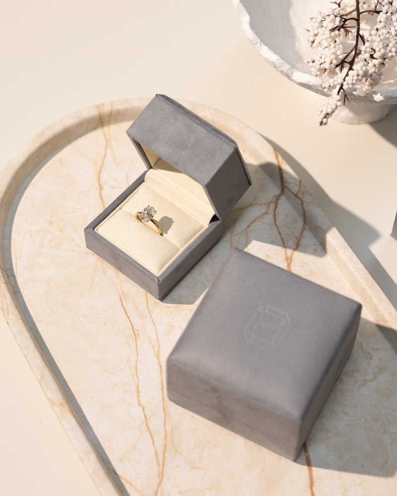 stylish & luxurious gry ring box with an oval diamond engagement ring on a marble tray